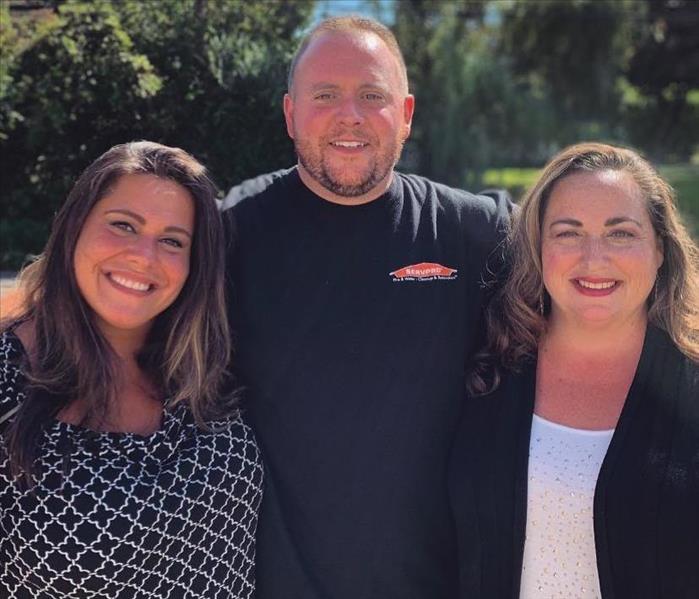 two female employees, one male employee standing outside together smiling